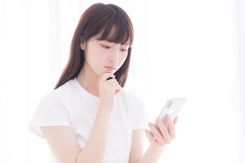 携帯を持って悩む女性